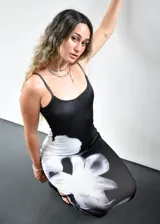 Vestido largo de corte ajustado, confeccionado en tela elastizada de color negro con un estampado floral grande en tono blanco y gris que recorre el lateral de la prenda. Presenta breteles finos y escote recto.
