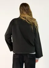 Chaqueta negra de algodón con diseño de volados en el frente, cierre de botones y bolsillos laterales.