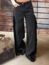 Pantalón de jean negro de corte amplio y tiro medio-alto. Presenta flecos laterales de cuero genuino a lo largo de las piernas.