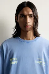 Camiseta relaxed fit de color celeste con efecto acid wash, cuello redondo y manga corta. Cuenta con estampa frontal con la inscripción "HOTEL STAFF" y "Escape Ibiza" en tonos amarillos.