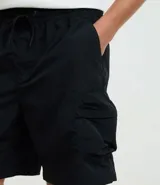 Bermuda cargo negra de tejido tecnológico (poliamida), con corte holgado, bolsillos laterales funcionales y cintura elástica con cordón ajustable.