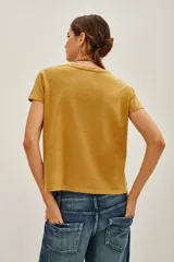 Remera de algodón color mostaza con estampa frontal estilo vintage que incluye un diseño de trompeta, piano y la inscripción '1983 Live Jazz Festival'. Presenta cuello redondo y mangas cortas.