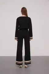 Pantalón negro de tejido de punto con corte palazzo y cintura alta. Presenta dos franjas horizontales color crema en el ruedo.