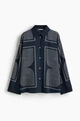 Camisa de sarga de corte oversized, color azul marino, con estampado geométrico de líneas blancas. Presenta cuello clásico, cierre frontal con botones, hombros caídos y mangas largas con puños abotonados.