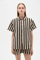 Camisa de algodón de corte holgado, con diseño de rayas verticales en colores negro y beige, cuello camisero y cierre frontal con botones.