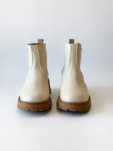 Bota corta de cuero vacuno con textura granulada, color crudo. Presenta cierre lateral metálico, suela track de goma en tono suela y tirador trasero.