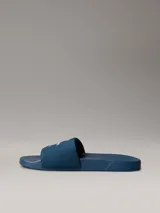 Chinelas de color azul con banda superior de material textil que presenta el logotipo de Calvin Klein bordado en blanco. La suela es ergonómica y antideslizante, con el nombre de la marca grabado en el lateral.