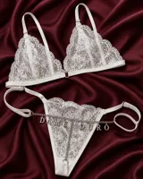 Conjunto de lencería de encaje blanco compuesto por un bralette triangular con tirantes regulables y una tanga con tiras ajustables, decorada con una cadena metálica con dijes que forman la frase "DAME DURO".
