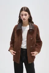 Chaqueta de gamuza color marrón con cuello camisero en cuero oscuro, cierre frontal con broches metálicos tipo gancho y bolsillos delanteros aplicados.