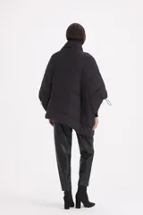 Campera tipo mantela acolchada de color negro, con cierre frontal cruzado, cuello alto y mangas amplias con puños elásticos ajustables. Presenta bolsillos laterales y un bolsillo frontal con cierre.