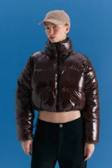 Campera puffer corta de acabado brillante en color marrón oscuro, con cuello alto, cierre frontal y diseño acolchado.