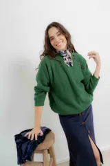 Sweater de punto color verde, con cuello redondo y detalle de cierre cruzado con botones en el hombro. Presenta un diseño holgado y mangas largas.