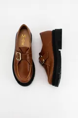 Mocasines de cuero color verde oliva con suela track negra de plataforma. Presentan una tira decorativa sobre el empeine con hebilla metálica dorada ajustable en el lateral.