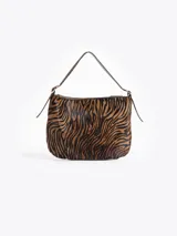 Cartera tipo hobo confeccionada en cuero con pelo vacuno estampado animal print. Presenta correa de hombro ajustable con detalles de hebillas metálicas en los laterales y cierre superior.
