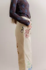 Pantalón de gabardina color crudo con estampado artístico de motivos botánicos y arquitectónicos. Presenta corte recto, tiro medio y bolsillos laterales.