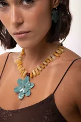 Collar corto con dije de flor doble en color turquesa, con pétalos texturados y pintados a mano. La cadena está compuesta por piedras naturales en tonos amarillos y naranjas, con cierre de acero quirúrgico ajustable.