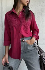 Camisa de color bordó con cuello clásico y cierre frontal de botones. Presenta un diseño distintivo con paneles de encaje bordado en la parte superior delantera, mangas largas con puños y un corte recto.