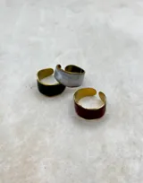 Anillo abierto de diseño minimalista con borde dorado y centro de resina con acabado perlado, disponible en colores negro, rojo y blanco.