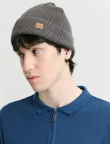 Gorro de punto inglés color gris, con diseño de doble vuelta y parche de cuero sintético con logo en el frente.