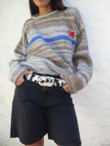 Cinturón de cuero sintético con estampado animal print de vaca en tonos marrones y blancos. Hebilla metálica plateada con logo grabado.