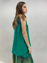 Blusa de satén con escote halter y cuello elevado anudado lateralmente. Presenta un diseño estampado degradado en tonos verde esmeralda y azul, con corte holgado y caída fluida.