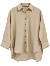 Camisa de manga larga color beige, corte oversize, con cuello camisero, cierre frontal de botones y detalles de volados sutiles en los puños.