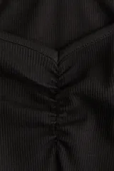 Top negro de manga corta, confeccionado en tejido acanalado, con escote tipo bote que deja los hombros descubiertos y detalle fruncido en el centro del busto.