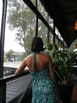 Vestido corto turquesa cubierto de lentejuelas brillantes, con escote en cascada, tirantes que se aten al cuello y volado en el ruedo.