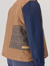 Campera de diseño híbrido con frente acolchado en color tostado, solapas y cuello en tejido de lana con patrón de cuadros tipo príncipe de gales, y mangas en paño de lana color azul marino. Cuenta con cierre frontal de botones.
