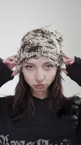 Gorro tipo beanie con diseño de tejido desmechado en tonos marrón y crudo.