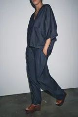 Camisa de tejido tipo denim azul oscuro, con escote pico, manga corta ancha y dos bolsillos de parche frontales. Cierre frontal con botones.