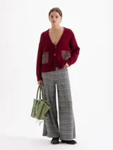 Pantalón de tiro alto con corte amplio y relajado, confeccionado en tejido de punto con estampado de cuadros tipo príncipe de gales. Presenta cintura elástica, bolsillos laterales con broches metálicos y botamangas amplias.