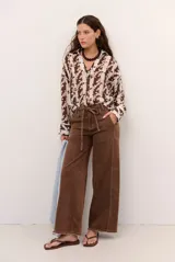 Jean tostado de corte wide leg, tiro medio con presillas y lazo ajustable en la cintura. Presenta bolsillos delanteros y traseros, costuras decorativas verticales y terminación desmechada en el ruedo.