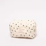 Neceser acolchado color crema con estampado de pequeños corazones negros. Presenta un cierre superior y una etiqueta tejida con texto en francés en color rojo.