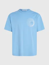 Remera de algodón en tono celeste claro, corte relajado y manga corta, con cuello redondo. Presenta un pequeño logo gráfico circular que simula un vinilo o disco en el lado izquierdo del pecho.