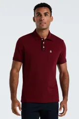 Chomba de piqué color bordó con cuello y puños con detalle de ribete en contraste. Presenta cierre frontal de tres botones y un bolsillo en el pecho con el logo de la marca bordado.