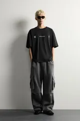 Pantalón jogger de corte relajado confeccionado en tejido de algodón compacto con elasticidad. Presenta cintura elástica ajustable con cordón, bolsillos laterales, bolsillos cargo con solapa en las piernas y detalle de pliegues en las rodillas.