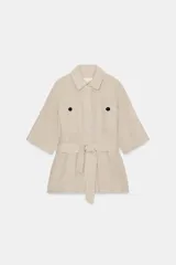 Chaqueta de estilo safari confeccionada en lino, color beige, con cuello solapa, manga corta y bolsillos delanteros de plastrón con botones negros. Incluye cinturón ajustable del mismo tejido y cierre frontal con botones ocultos.