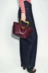 Bolso de mano tipo saco, color borgoña, con asa superior metálica con forma de corazón martillado en tono dorado. Incluye un compartimento interior extraíble y cierre mediante botón metálico.