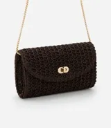 Cartera pequeña de rafia color marrón oscuro con textura de efecto paja. Posee una correa de cadena dorada para uso transversal y un cierre frontal de metal tipo locker.