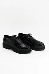 Zapatos tipo wallabee de cuero charolado negro, con cordones al tono y suela track de goma con plataforma.