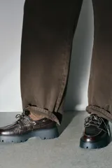 Mocasín de cuero marrón con diseño tipo náutico, presenta ojales metálicos laterales con cordones y suela de plataforma dentada en color negro.