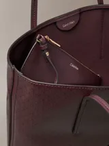 Cartera tote pequeña Calvin Klein de color bordó, con estampado geométrico de monograma, doble asa de mano y monedero o cartera mini interior a juego con cierre y logo dorado.