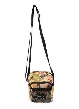 Morral Billabong modelo Pass By con estampado tropical de hojas en tonos verde, beige y rosado, con correa ajustable negra y bolsillo frontal de red con etiqueta de la marca.