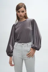 Blusa de terciopelo gris con acabado brillante, cuello redondo y mangas largas abullonadas con puños elásticos.