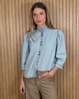 Camisa de denim claro con cuello alto fruncido, mangas abullonadas tres cuartos y cierre frontal de botones.