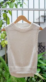 Chaleco tejido de punto en color crudo, con cuello alto y diseño sin mangas. Presenta una textura de punto grueso y corte recto.