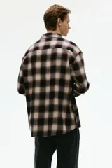 Camisa de manga larga confeccionada en franela de algodón suave, con diseño de cuadros en tonos marrones y beige. Presenta cuello inglés, cierre frontal con botones y bajo redondeado.