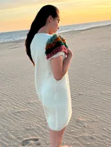 Vestido midi de punto color marfil, confeccionado en lana merino, con mangas cortas decoradas con flecos mullidos de varios colores y trenzas verticales al frente.