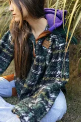 Buzo tipo canguro de corte oversize, confeccionado en paño de lana con diseño de rayas horizontales en tonos marrón, blanco y azul. Presenta una capucha amplia y un cuello de piel sintética en color verde oscuro.